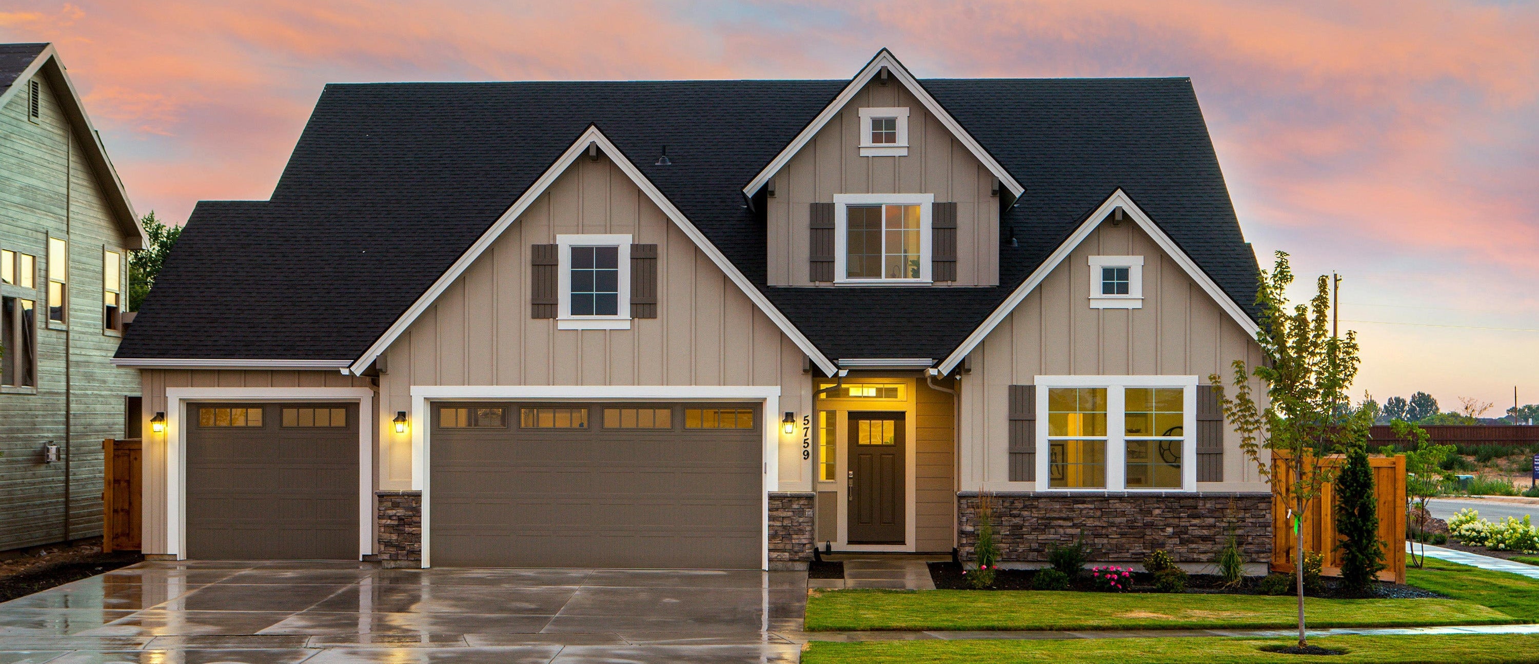 Two-story house with a two-car garage under a colorful sunset sky.